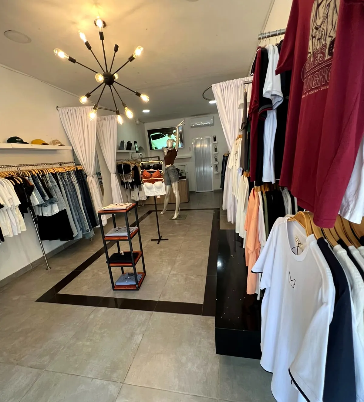 Interior de la tienda Joshelo con lámpara de bombillos, camisetas colgadas y probadores con cortinas blancas