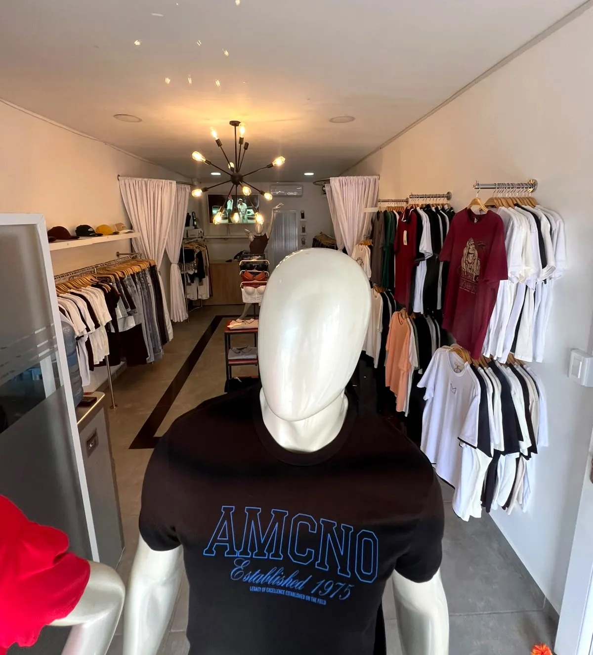 Pasillo de la tienda con maniquí, camisetas en las paredes y gorras en la repisa